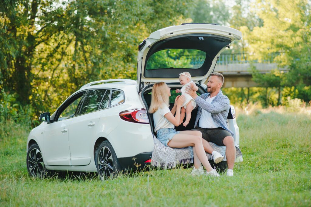 Parents playing with baby while sitting in open car trunk on a family road trip