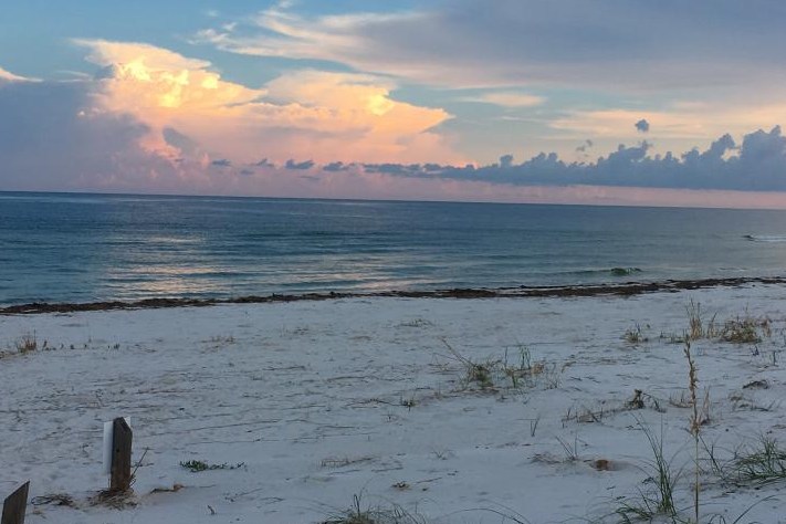 St. George Island State Park, Florida. White sand beach with blue water with sun setting behind clouds.
