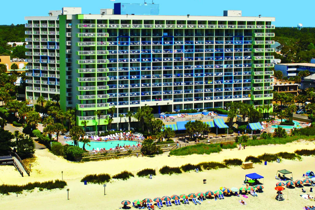 Aerial view of the Coral Beach Resort Hotel & Suites from the beach side looking at rear of hotel with pools on left and right of hotel