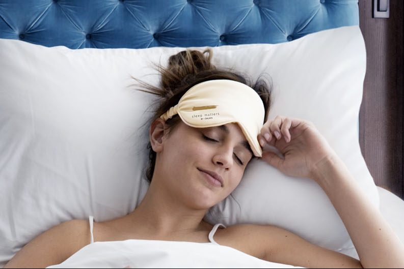 Woman just waking up from a deep sleep, wearing an eyemask that says Langham Sleep Matters By Chuan