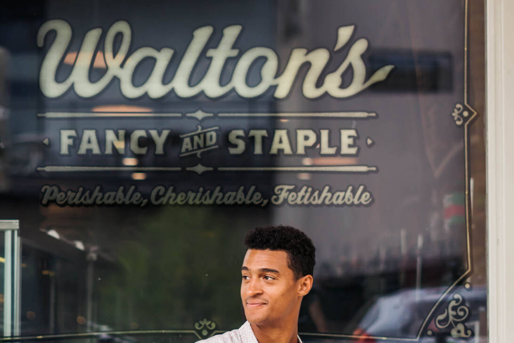 Man sitting out front of Walton's Fancy and Staple