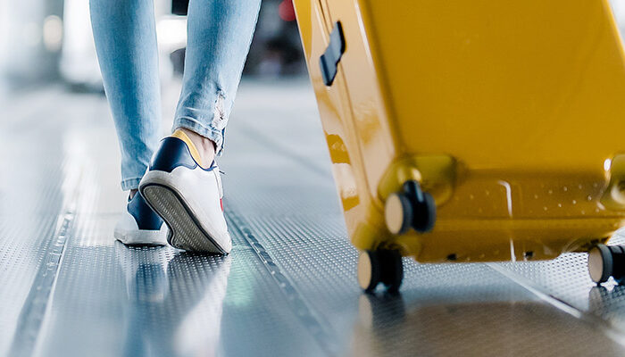 Close up of a person's legs and feet as they walk through the airport pulling a yellow suitcase