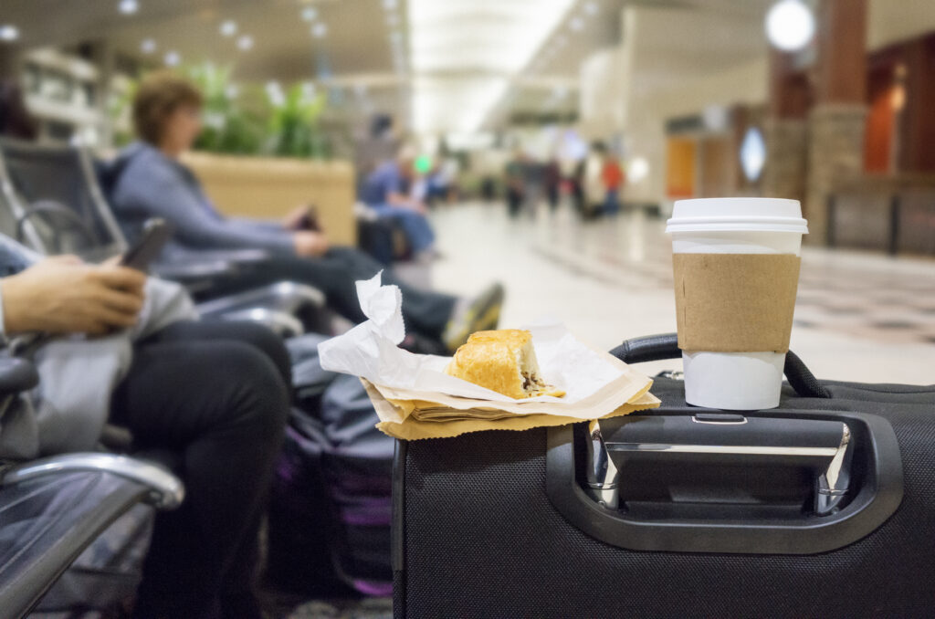 Close up of a takeaway cup of coffee and a half-eaten breakfast pastry sitting on top of a suitcase in an airport