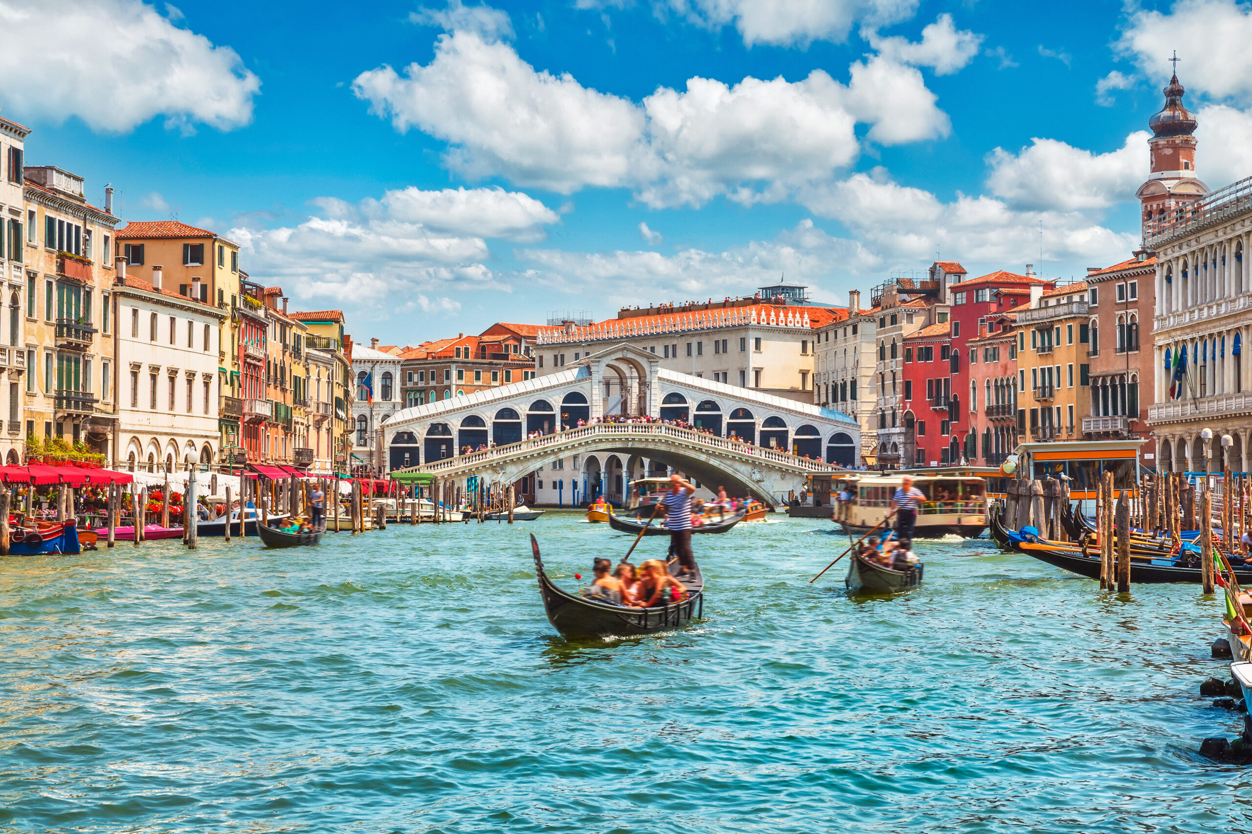 Person navigating a gondola in front of the Bridge Rialto on Grand Canal in Venice, Italy on a clear day