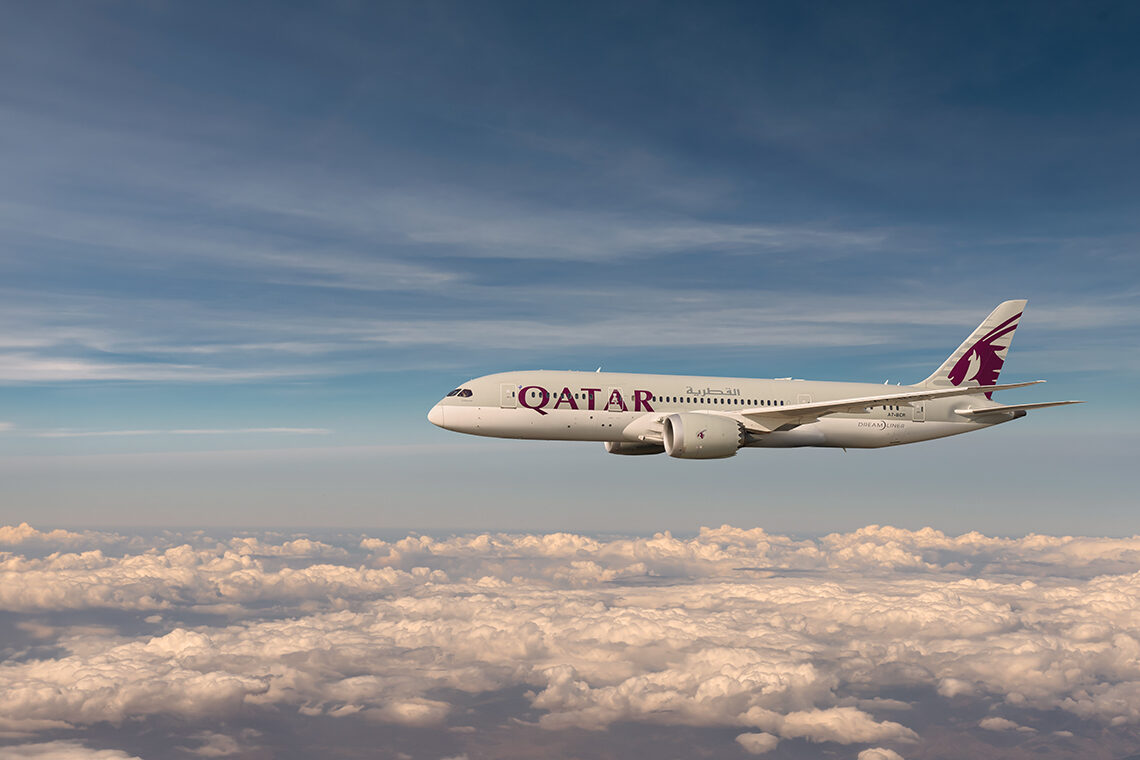 A Qatar Airways aircraft flying through the sky at dusk