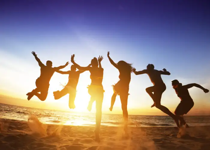 Silhouettes of friends jumping into the ocean at sunset