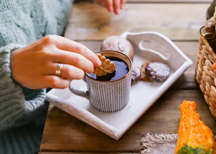 Close up of a woman dipping a cookie into a mug of coffee on a table set up with fall decor and desserts