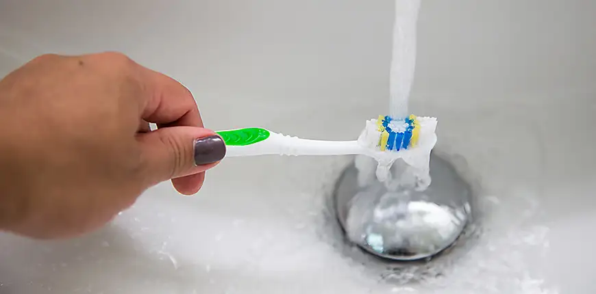 person gets toothbrush wet in sink