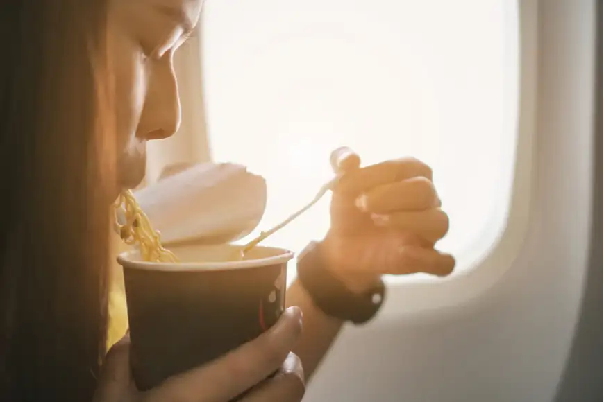 woman eating noodles on a plane.