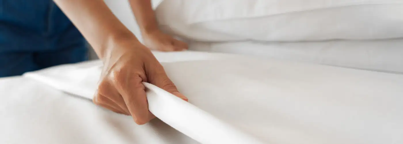 Close up of hand making hotel bed with white sheets
