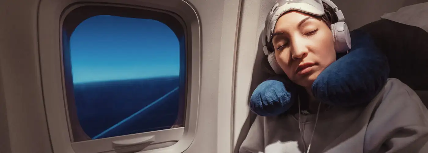 Woman sleeping on plane with neck rest, eye mask, and headphones