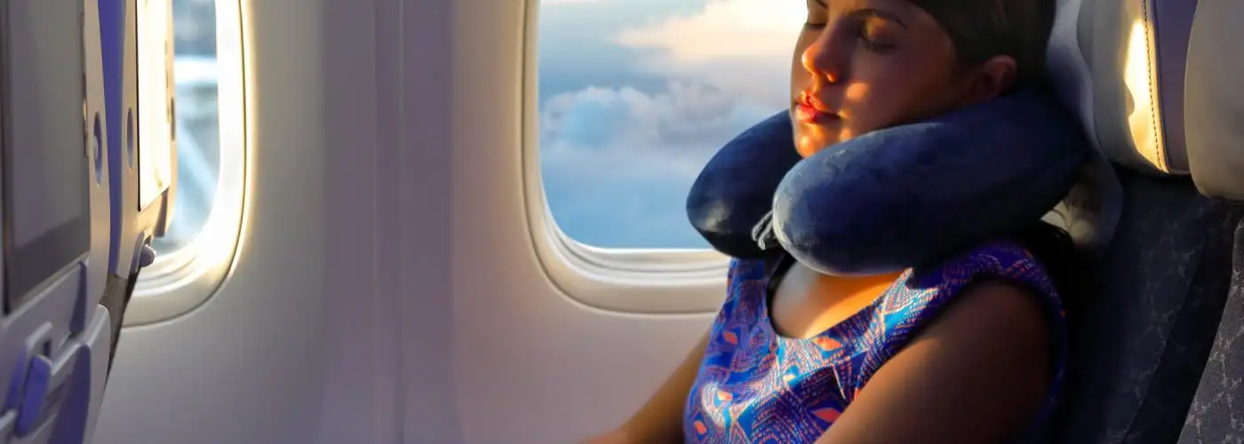 young woman sleeps with a pillow under her head at the window of the airplane during the flight