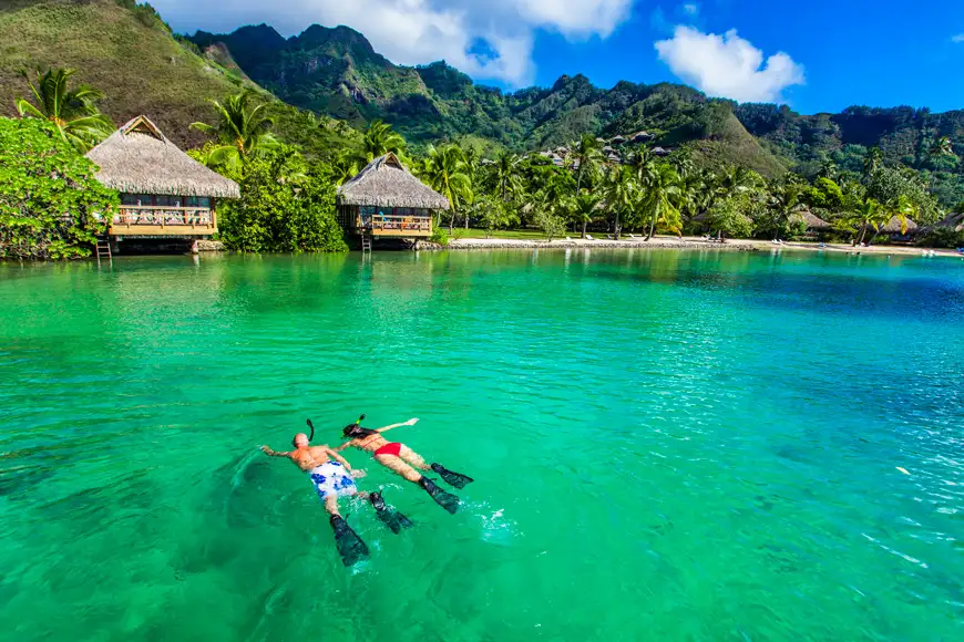 Young couple snorkeling over reef next to resort on a tropical island with over-water villas