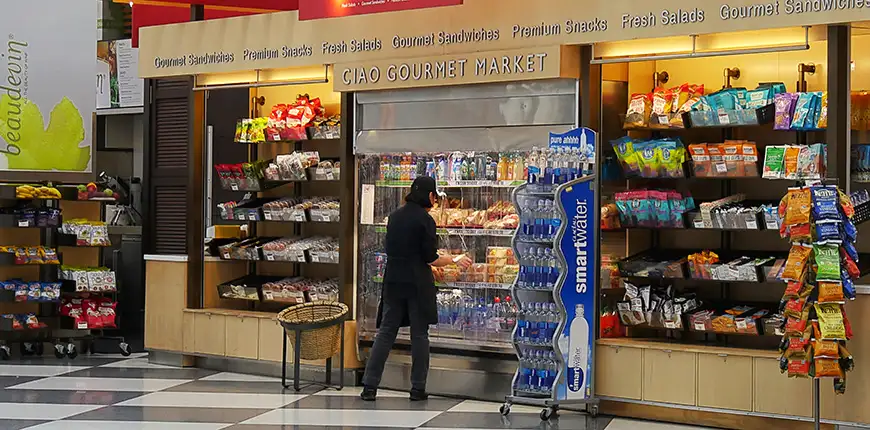A woman arranges beverage displays inside at a gourmet market the airport