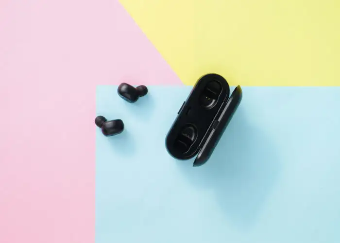Aerial view of black wireless earbuds and charging case on a pink, yellow, and blue pastel backdrop