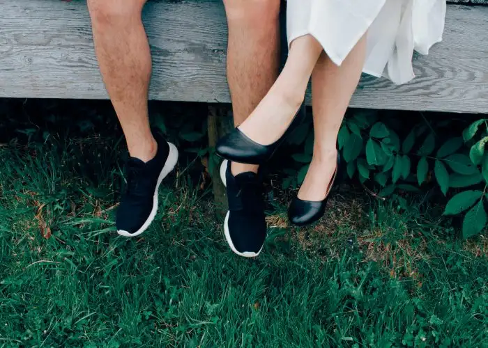 male and female sitting with grass background wearing sneakers and slip on shoe