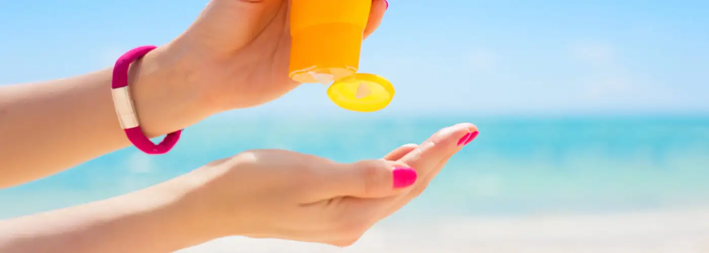 Close up of person squeezing sunscreen from an orange bottle into their open hand at the beach
