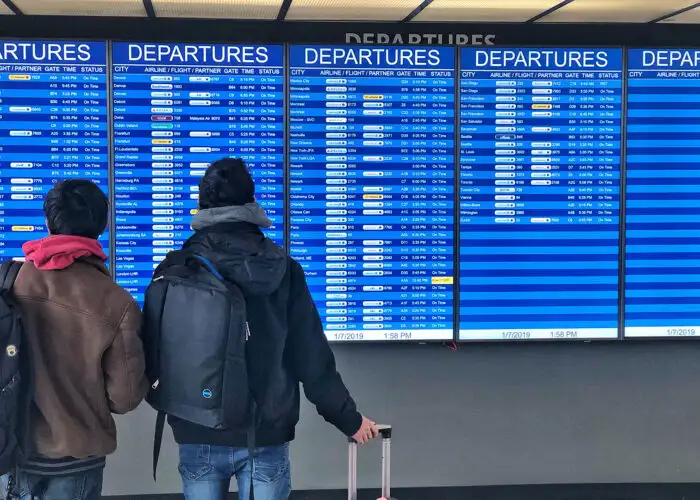 travelers in front of airport departure board
