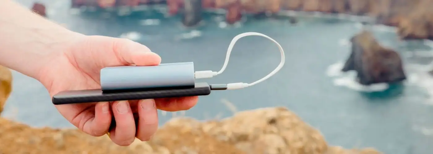 hand holding smartphone portable charger with ocean in background.