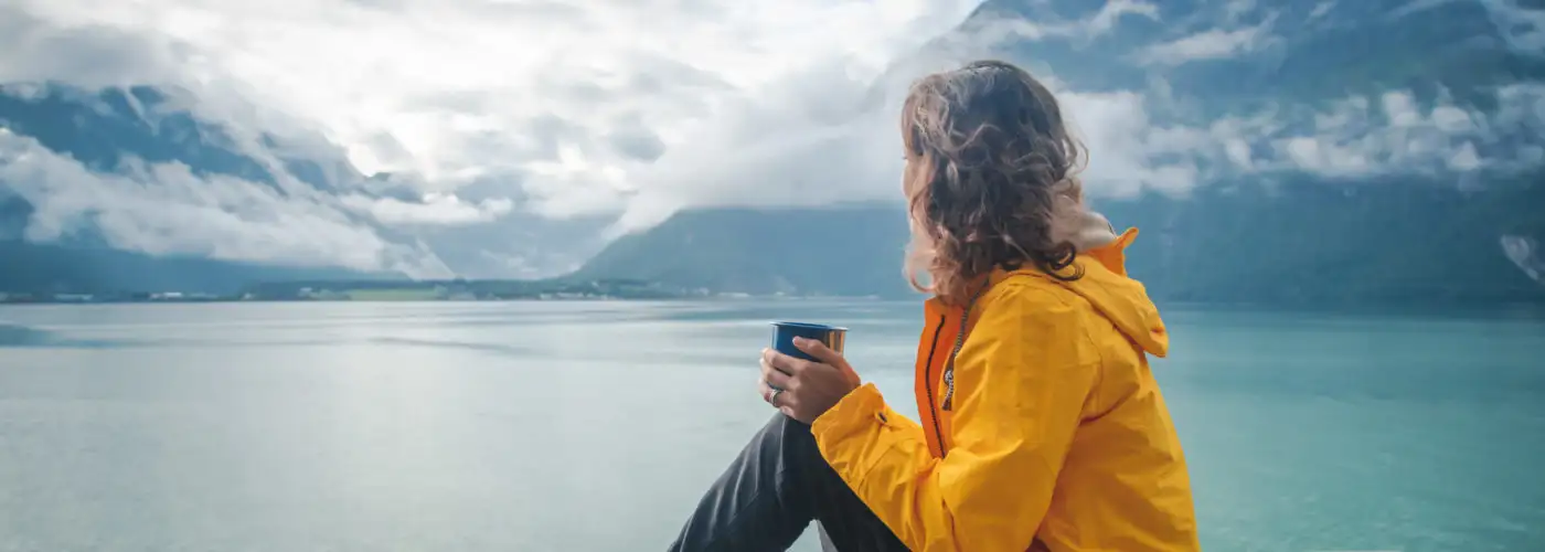 Woman drinking from mug and looking out on fjord