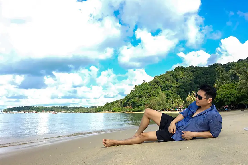 Asian man lying down on the beach relaxing and seeing beautiful sea view on his holidays on paradise island.