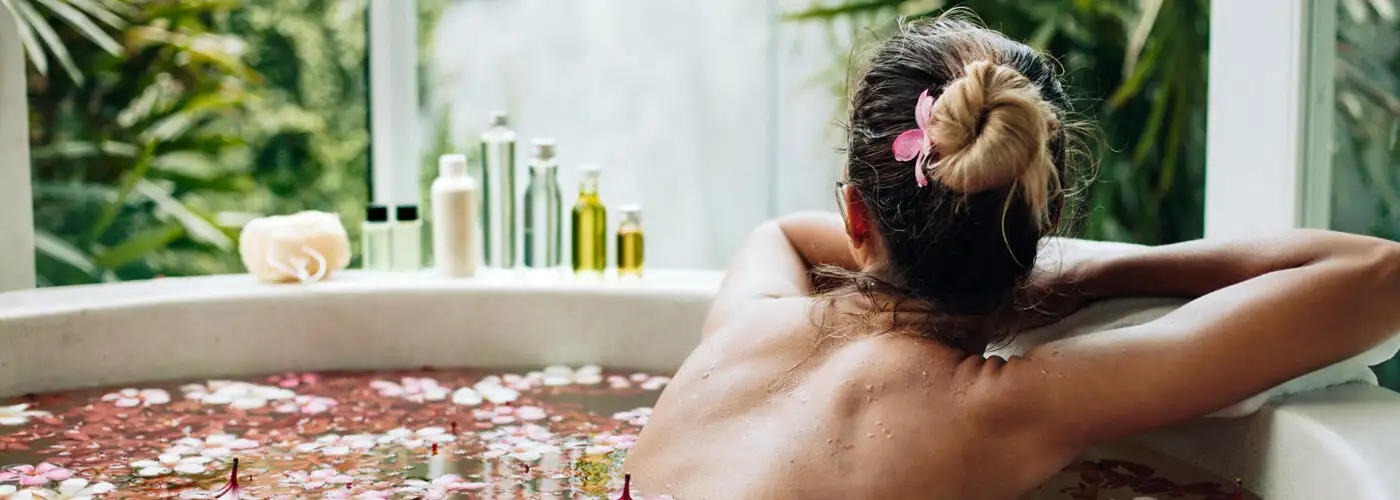 women in bath filled with rose petals and essential oils on the side