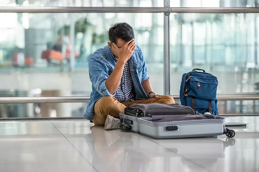 man sitting on floor at airport with open luggage lost item