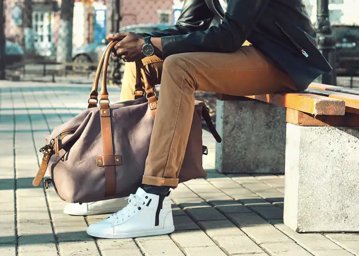 man holding weekender bag sitting bench city