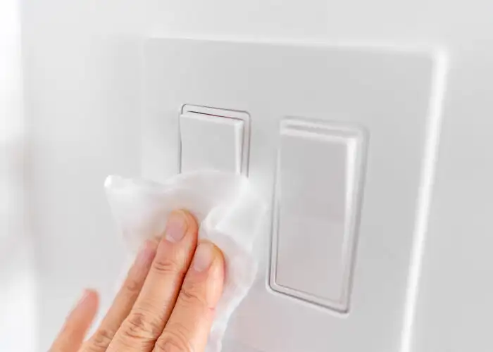 hands wiping lightswitch with disinfectant wipes