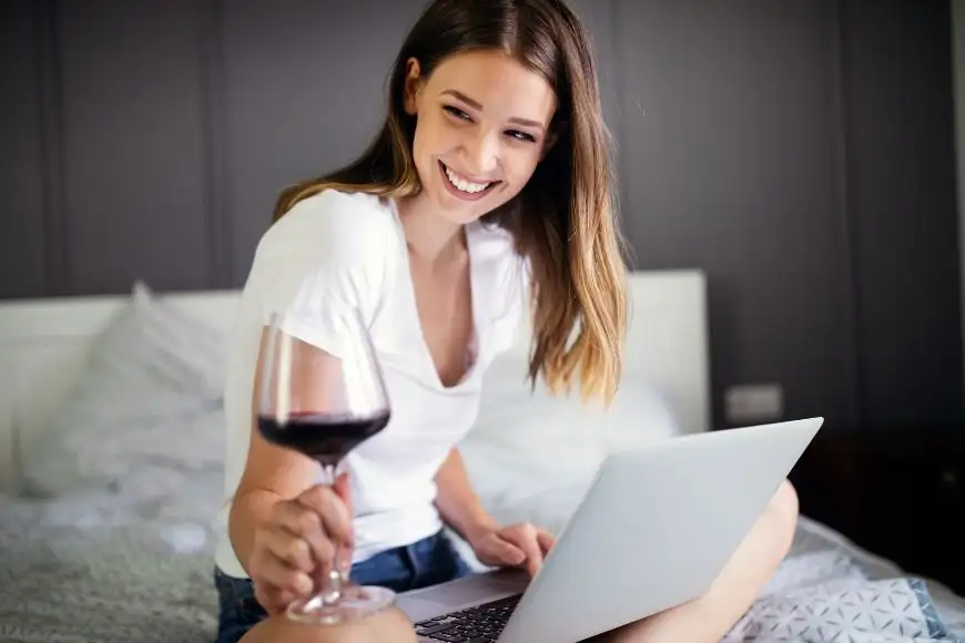young woman with wine on laptop at home.