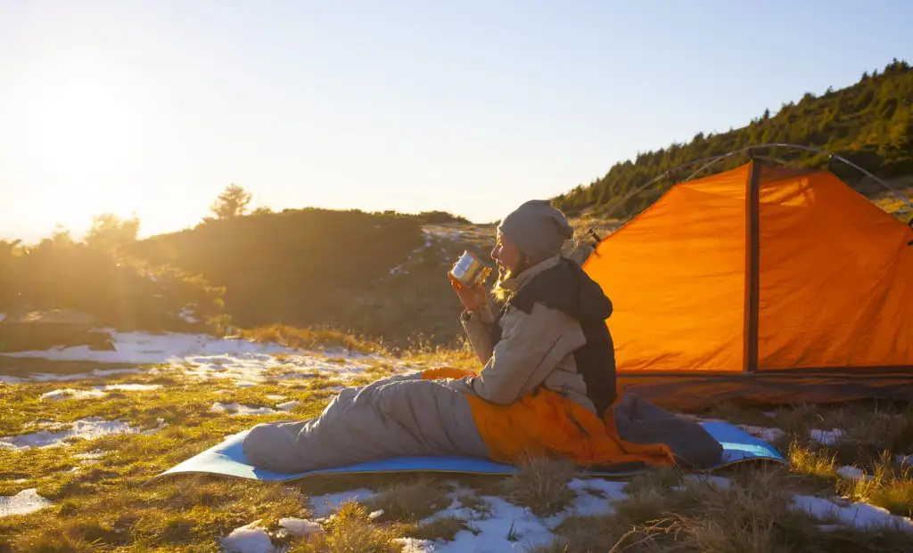 Woman drinking from a metal cup in a sleeping bag