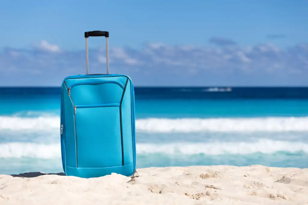 Blue suitcase on the sand in front of the ocean