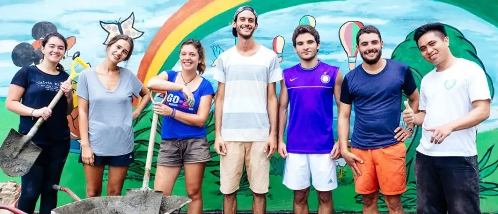 Group of young travelers holding shovels, posing in front of a colorful mural