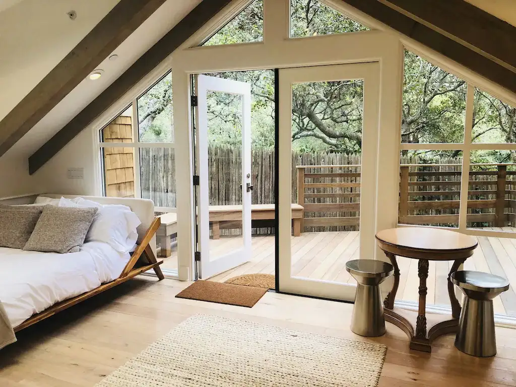 An a-frame bedroom with an open door leading out onto a wood deck area in Carmel-by-the-Sea, California