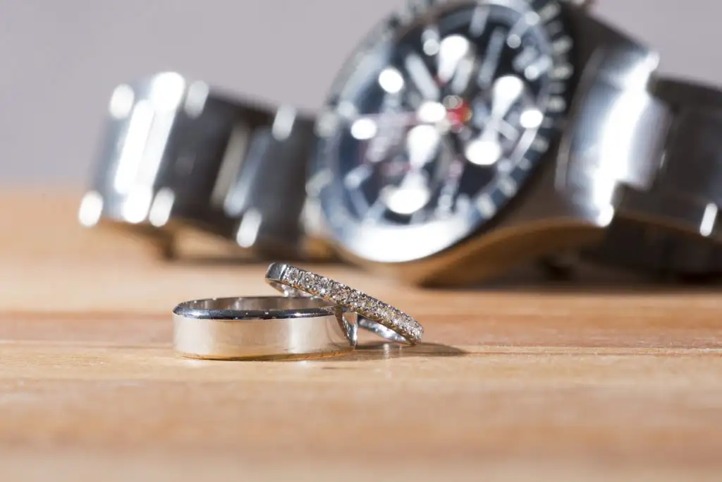 Silver watch and wedding rings on a wooden table