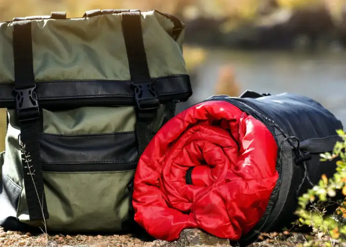 A sleeping bag and backpack on the ground in the woods
