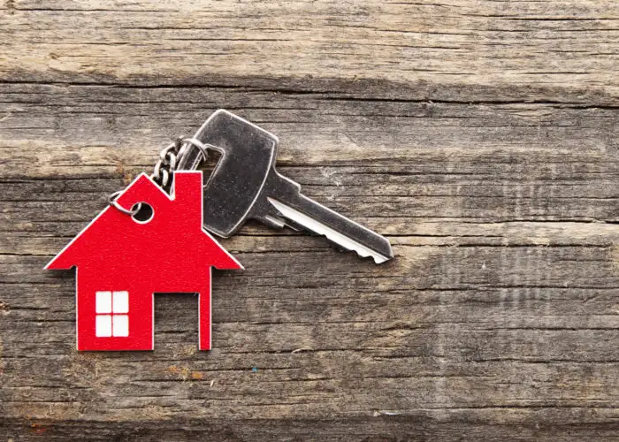 House key with red house-shaped keychain on a wooden background