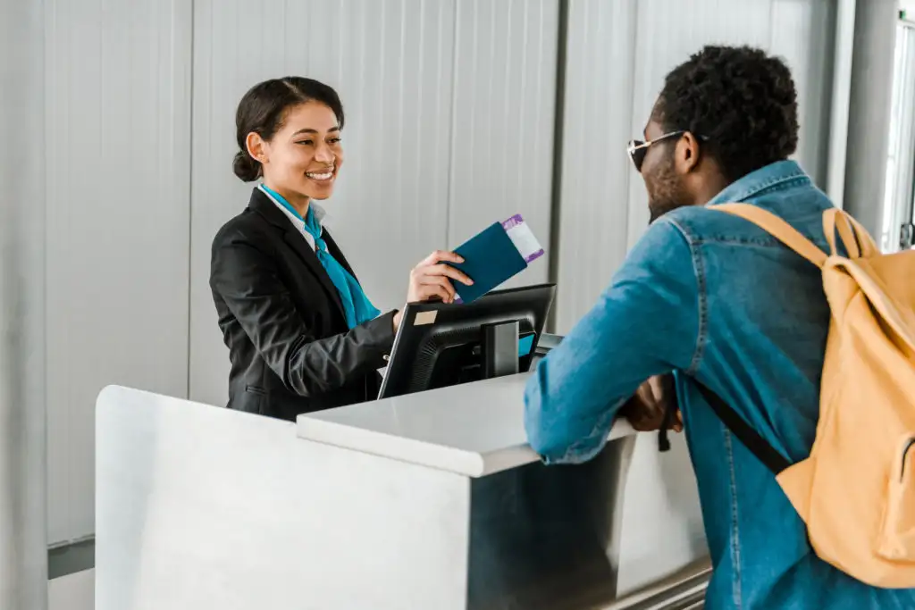 Flight attendant hands passport and boarding pass back to tourist with backpack