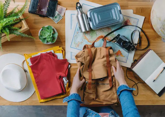 Hands packing a backpack with sustainable travel gear surrounding them