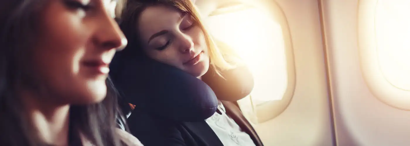 Woman sleeping using a neck pillow in a window seat on an airplane
