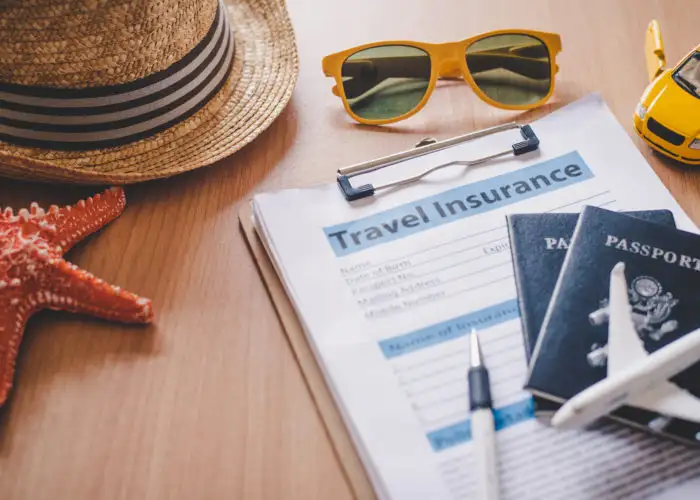 Travel insurance forms on a table surrounding by travel items