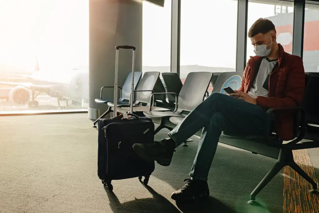 Man waiting on his phone with suitcase at airport terminal