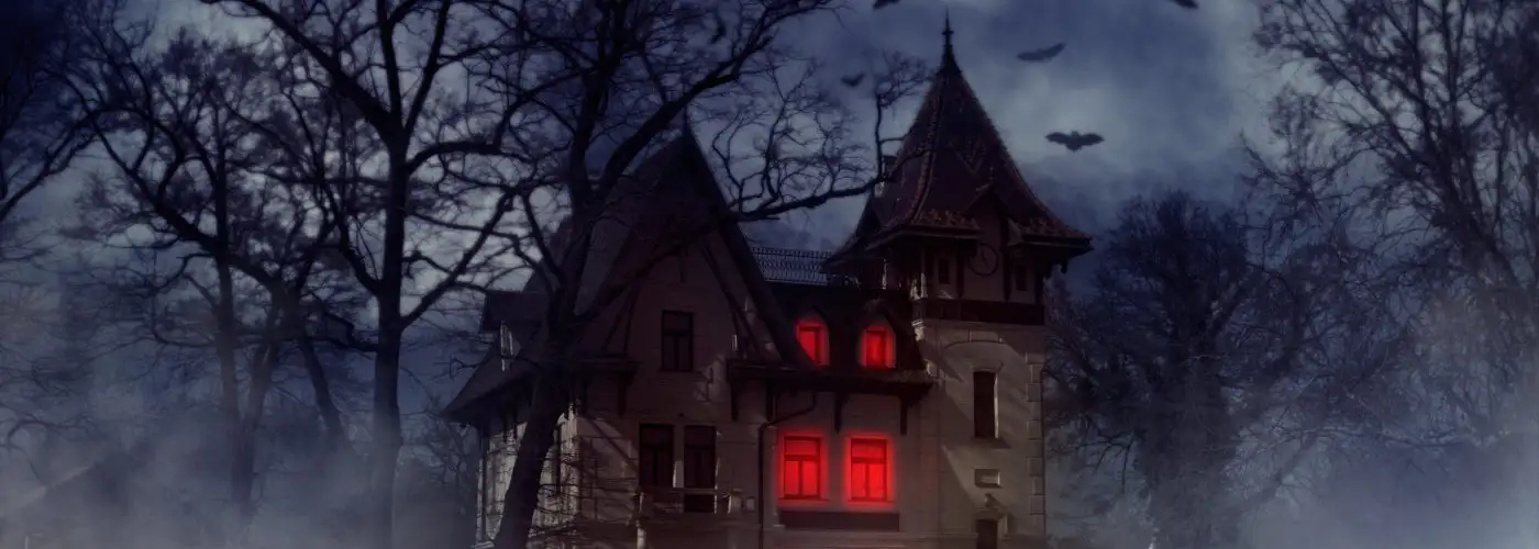 Haunted house on a hill with red lights shining inside and bats flying overhead