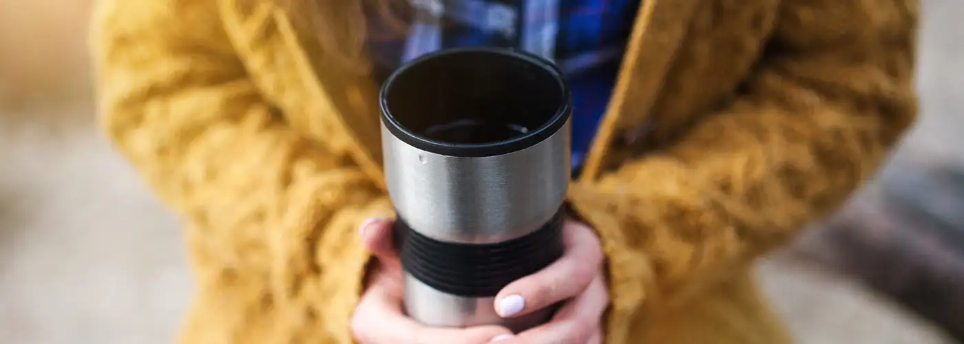 Woman holding hot travel mug of coffee