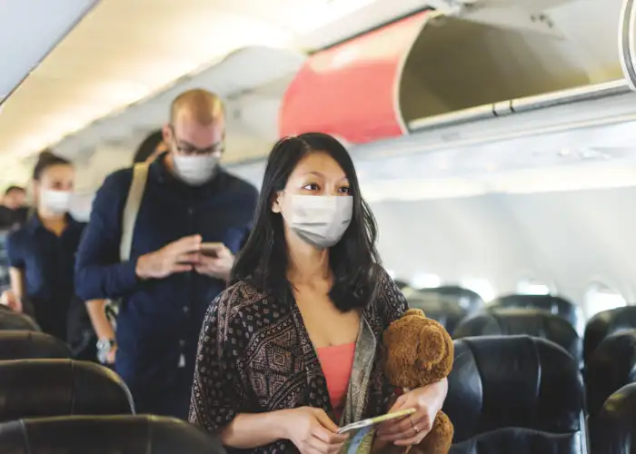 A line of people looking for their seats on the plane and wearing protective face masks