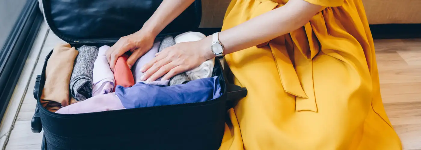 Close up of person in yellow dress packing a suitcase
