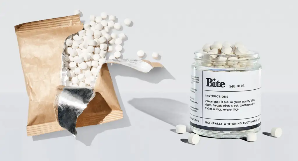 A glass jar and compostable paper package of Bite Toothpaste Bits