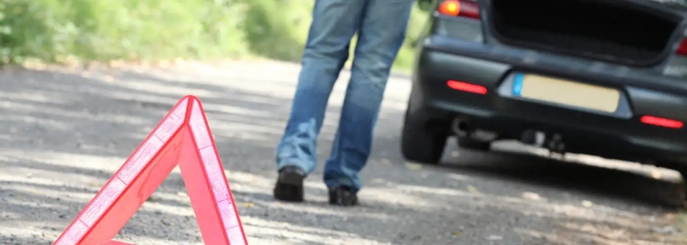 Man setting out hazard triangle from car emergency kit at breakdown
