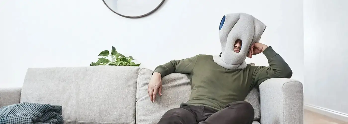 Man wearing an Ostrichpillow and lounging on a couch