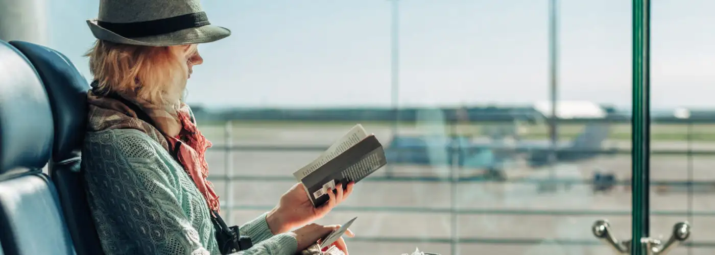 Woman reading book in front of a large window at an airport